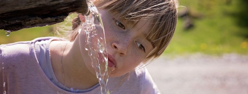 An image of a little girl with dehydration drinking water from a wooden pitcher.